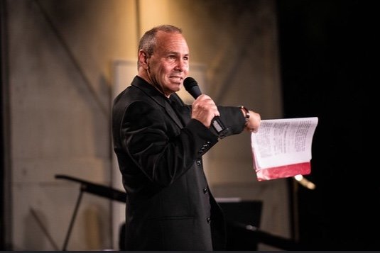 Adam Matalon speaking on stage with a microphone